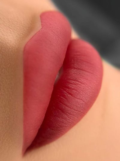 Close-up image showing a professional applying lip blush micropigmentation on a client’s lips. The procedure is performed with precision, enhancing the natural shape and color of the lips with semi-permanent pigment for a fuller, more defined look